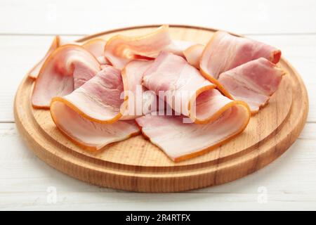 Pancetta cruda fresca tagliata sul tagliere di legno su bianco. Vista dall'alto. Foto Stock