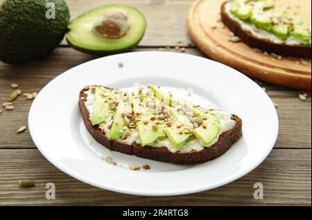 Panino di avocado su pane di segale scuro con avocado fresco a fette su fondo marrone. Vista dall'alto Foto Stock