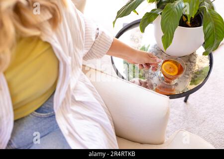 A metà della più grande donna caucasica giovani collocando la tazza da tè da pianta in vaso su tavolo di vetro a casa Foto Stock