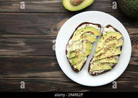 Panino di avocado su pane di segale scuro con avocado fresco a fette su fondo marrone. Vista dall'alto Foto Stock