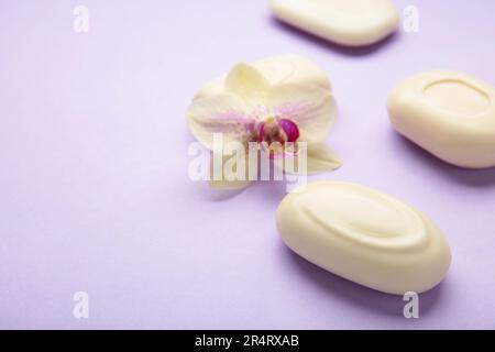 Saponi bianchi diversi con fiori. Un sacco di sapone solido per l'igiene e la pulizia su sfondo viola. Vista dall'alto. Foto Stock