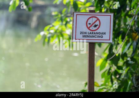 La traduzione in inglese per le parole malesi è il segno 'non pescare' che si trova accanto al lago. Foto Stock