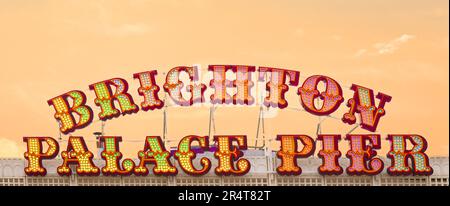 Brighton, Regno Unito - Maggio 19 2019: Brighton Palace Pier firma in colorate luci stile fiera in uno stile poster panorama con uno sfondo arancione cielo. Foto Stock