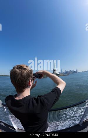 STATI UNITI, New York, turista che fa una foto al cellulare della statua della libertà. Foto Stock