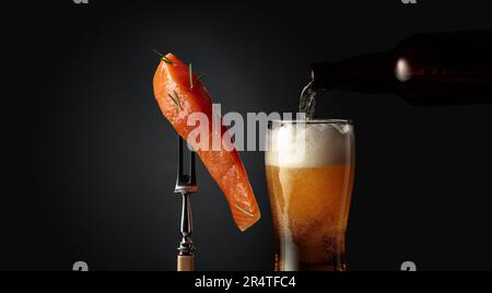 Salmone affumicato con rosmarino su forchetta e un bicchiere di birra su fondo scuro. La birra viene versata da una bottiglia in un bicchiere. Spazio di copia. Foto Stock