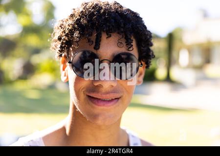 Primo piano ritratto di un bel giovane biraciale che indossa occhiali da sole e si posa in cortile Foto Stock
