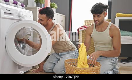 Due uomini si accoppiano sorridendo e si lavano i vestiti nella lavanderia Foto Stock