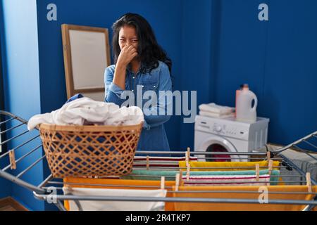 Giovane donna asiatica appendere abiti a clothesline odore qualcosa di puzzolente e disgustoso, odore intollerabile, tenendo il respiro con le dita sul naso. male Foto Stock