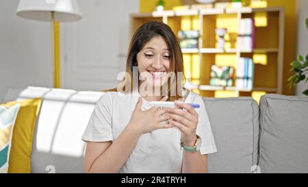 Giovane donna bionda che tiene test di gravidanza con espressione a sorpresa a casa Foto Stock