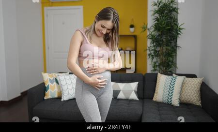 Giovane donna incinta che indossa abbigliamento sportivo che tocca la pancia a casa Foto Stock