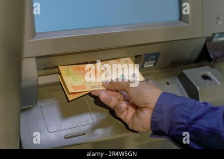 Particolare della mano di un uomo che prende le fatture del pesos argentino da un ATM. Foto Stock