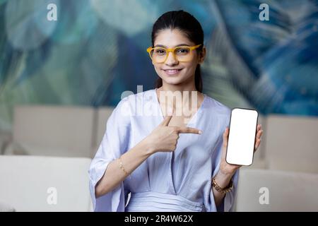 Pubblicità mobile. Felice bella donna che mostra Big Blank smartphone alla fotocamera mentre si siede sul divano a casa, giovane donna dimostrazione Telefono Wi Foto Stock