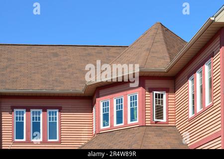 Una grande torretta con più lunghe finestre strette, di colore bianco e rosa. Il tetto presenta scandole marroni e si unisce a parti dell'edificio. Foto Stock