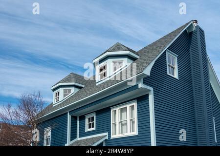 La vista esterna di due dormitori poligonali su un moderno tetto blu di una casa in legno. I dormitori su più lati sono dotati di tre finestre sospese doppie. Foto Stock