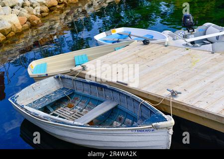 Piccole barche dixie dingy in fibra di vetro bianca ormeggiate ad un pontile galleggiante in legno. Lo skiff viene utilizzato per il trasporto come tender tra navi in un molo. Foto Stock