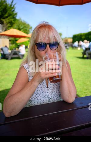 Donna che beve birra in un pub giardino Foto Stock