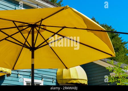 Grandi ombrelloni estivi in nylon da patio, di colore giallo, aperti con supporti in legno marrone. Lo sfondo è un cielo blu brillante. Il sole splende Foto Stock