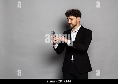 Uomo che fa selfie sulla fotocamera dello smartphone, blogger che comunica, registra video per i seguaci, agita la mano, saluta, indossa abiti in stile ufficiale. Foto Stock