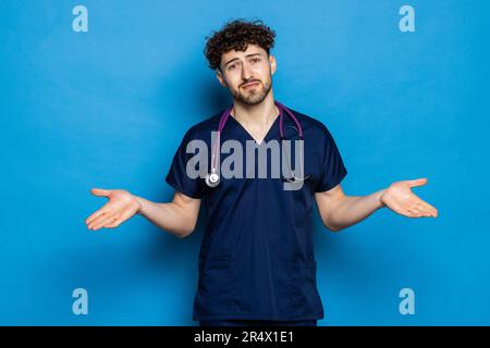 Giovane bel medico uomo con barba indossare cappotto e occhiali su sfondo blu confondere e meraviglia circa la domanda. Incerto con dubbio, pensando w Foto Stock