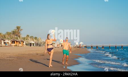 Antalya; Turchia-Settembre 11; 2022: Giovane coppia che gioca a Beach tennis in riva al mare. Persone che prendono il sole, nuotano o camminano sullo sfondo. Antalya Foto Stock