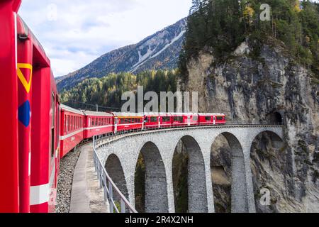 Filisur Svizzera - Ottobre 31. 2021: Un treno passeggeri rosso dalla Ferrovia Retica passando sul famoso Viadotto Landwasser. Foto Stock