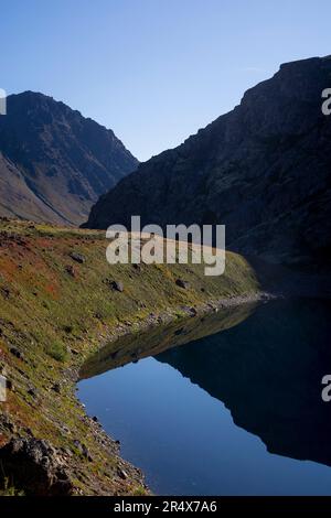 Vista ravvicinata di un lago alpino in autunno con la silhouette delle montagne Chugach contro un cielo blu nel parco statale di Chugach Foto Stock