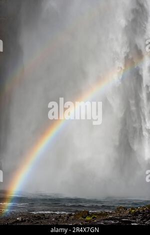 L'acqua che sgorga da una cascata con l'arcobaleno; Islanda Foto Stock