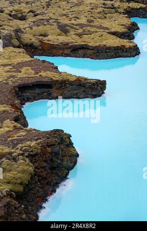 Splendida vista aerea dell'acqua blu turchese che crea un contrasto dinamico con i campi di lava coperti di muschio lungo la costa dell'Islanda meridionale Foto Stock