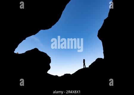 Silhouette di una donna contro un cielo blu, esplorando i canyon e il paesaggio di Thorsmork, un'area di eccezionale bellezza nel sud dell'Islanda Foto Stock