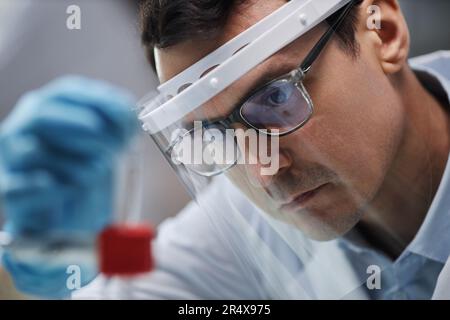 Primo piano di uno scienziato maschio che indossa una visiera protettiva in laboratorio mentre si eseguono esperimenti con liquidi chimici Foto Stock