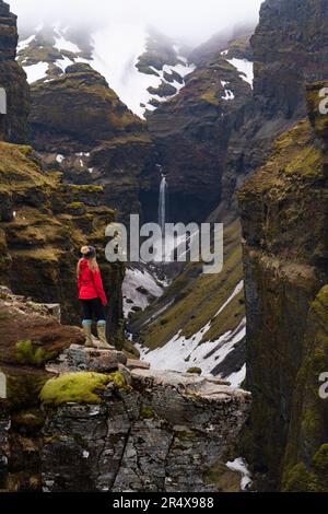 Donna in piedi e affacciata sul Mulagljufur Canyon, un paradiso per escursionisti, che guarda una vista incredibile di una cascata e delle scogliere coperte di muschio Foto Stock