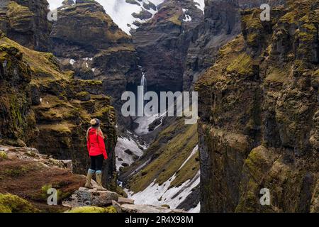 Donna in piedi e affacciata sul Mulagljufur Canyon, un paradiso per escursionisti, che guarda una vista incredibile di una cascata e delle scogliere coperte di muschio Foto Stock