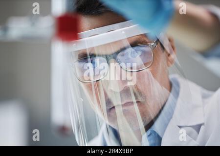 Primo piano di uno scienziato maschio che indossa una visiera protettiva in laboratorio mentre si eseguono esperimenti con la provetta Foto Stock