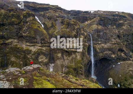 Donna in piedi e affacciata sul Mulagljufur Canyon, un paradiso per escursionisti, che guarda una vista incredibile di una cascata e delle scogliere coperte di muschio Foto Stock