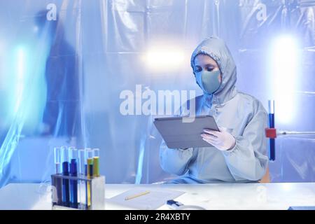 Scienziato femminile che indossa tuta protettiva completa che lavora alla scrivania nella zona di dange a rischio biologico, spazio copia Foto Stock