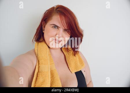 Selfie ritratto di più dimensione giovane donna latina di etnia argentina con capelli rossi corti è in piedi sorridente e guardando la fotocamera su bianco b Foto Stock