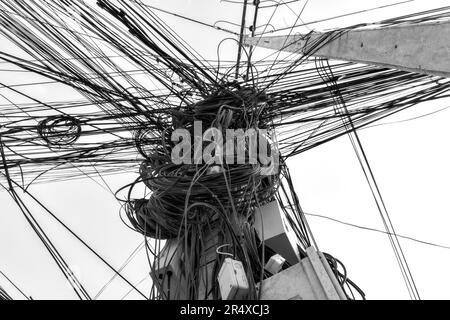 Un gruppo di fili e cavi impigliati su un palo, catturando l'intricata e caotica rete di linee elettriche asiatiche. Foto Stock