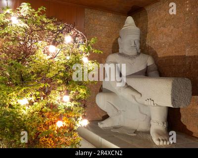 Scultura indù di un uomo e cespugli decorati con luci decorative. Foto Stock