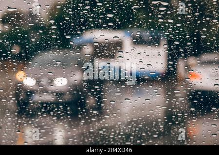 Sfondo città piovosa. Auto in movimento e autobus visto dalla finestra coperta da raindrop di auto di passaggio. Gocce di pioggia sul vetro della finestra. Messa a fuoco selettiva Foto Stock