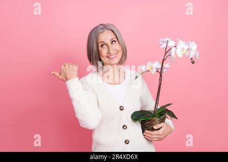 Foto a dimensione piena di attraente donna anziana punto look vuoto spazio orchidea vestito elegante vestiti bianchi isolato su sfondo di colore rosa Foto Stock