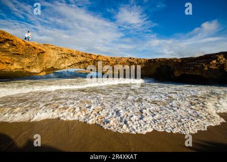 Il surf si snoda sotto un arco di roccia naturale.; paese di Aruba Foto Stock