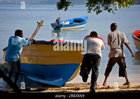 I pescatori spingono una barca appena pulita e dipinta in acqua; Bluefields Bay, Giamaica Foto Stock