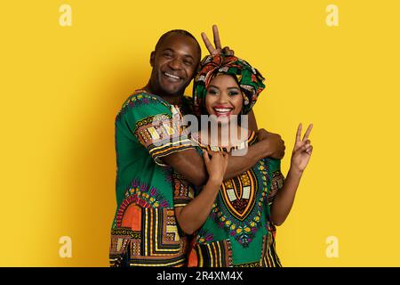 Divertente coppia nera gioiosa in costumi africani sul giallo Foto Stock