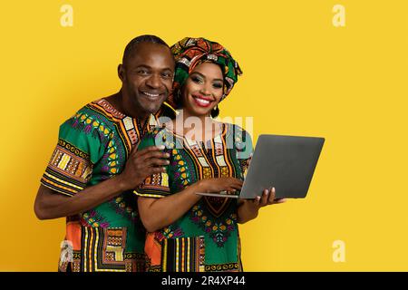 Bella coppia nera che controlla il contenuto sul notebook, sfondo giallo Foto Stock