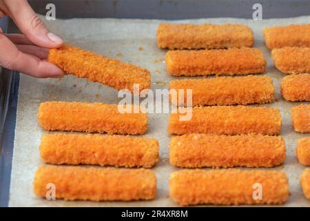 La mano distende le dita di pesce sulla carta da frittura. Il concetto di frittura di pesce bastone nel forno. Vista laterale. Foto Stock