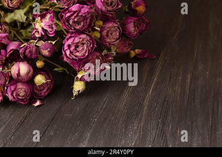 Bouquet di rose rosa secche su uno sfondo di legno scuro primo piano. Concetto di solitudine o età. Tristezza, amore infelice. Foto Stock