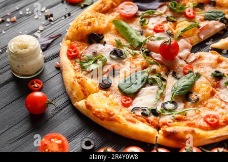 Pizza a jerky, formaggio, olive, salsa, spezie e verdure fresche su sfondo di legno scuro. Cucina italiana. Foto Stock