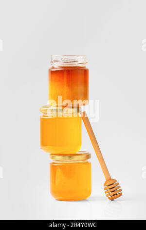 Miele in vasetti di vetro con cucchiaia. Miele biologico in vasetti su fondo bianco. Vasi aperti e chiusi con miele uno sopra isolamento. Foto Stock