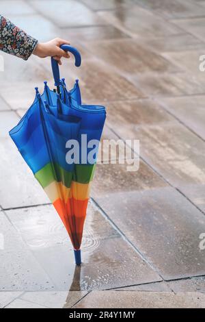 Ombrello per bambini sul marciapiede contro la strada bagnata. Nessuno. Primo piano di un ombrello strippy arcobaleno Foto Stock