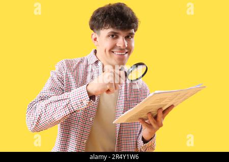 Giovane uomo con lente di ingrandimento e giornale su sfondo giallo Foto Stock